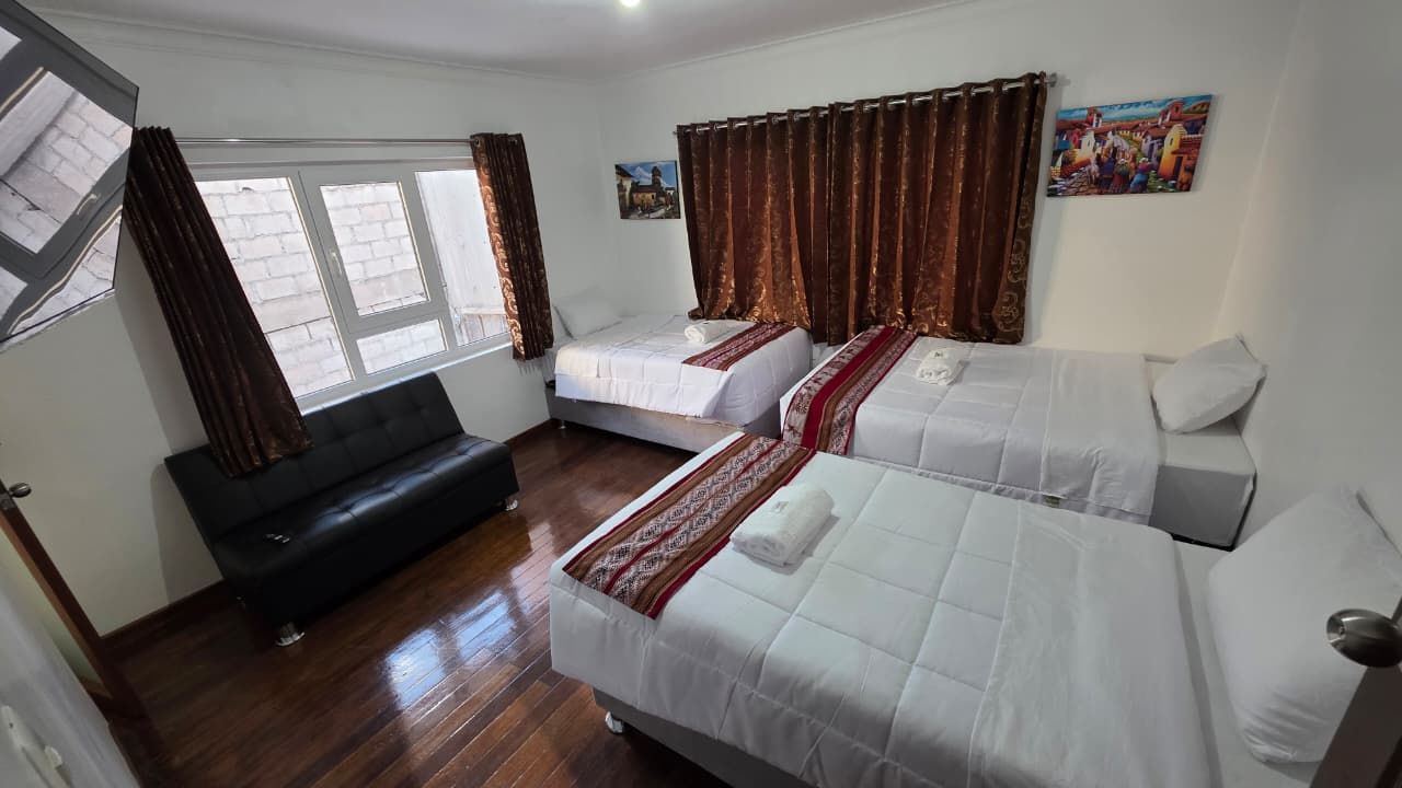 Habitación de hotel con dos camas, un sofá y un ventanal con cortinas.