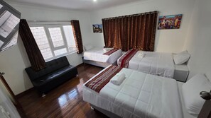 Habitación de hotel con dos camas, un sofá y un ventanal con cortinas.
