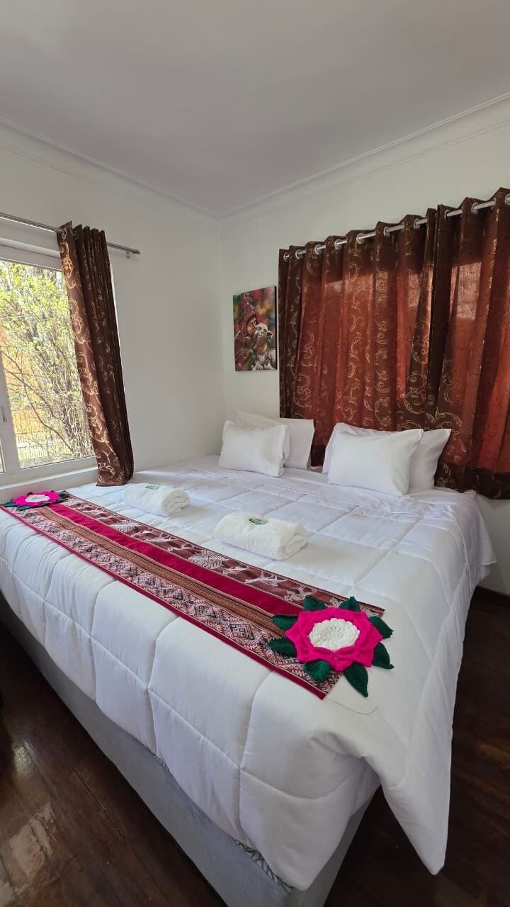 Ein Hotelzimmer mit einem großen Bett, zwei Kissen, einem Fenster mit Vorhängen und einem Gemälde an der Wand.
