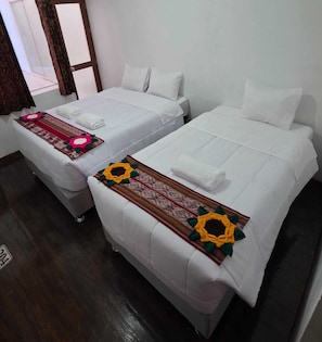 Two single beds with white linens and decorative pillows, a wooden door, and a patterned rug. - Cusco Inka Sky (Cusco)