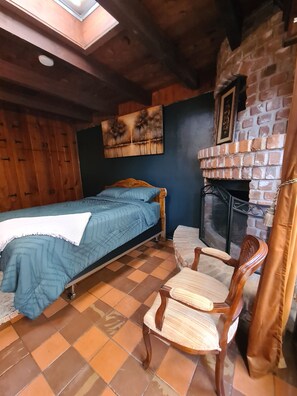 Ein Zimmer mit einem Bett, einem Sessel, einem Kamin und einem Bild an der Wand.