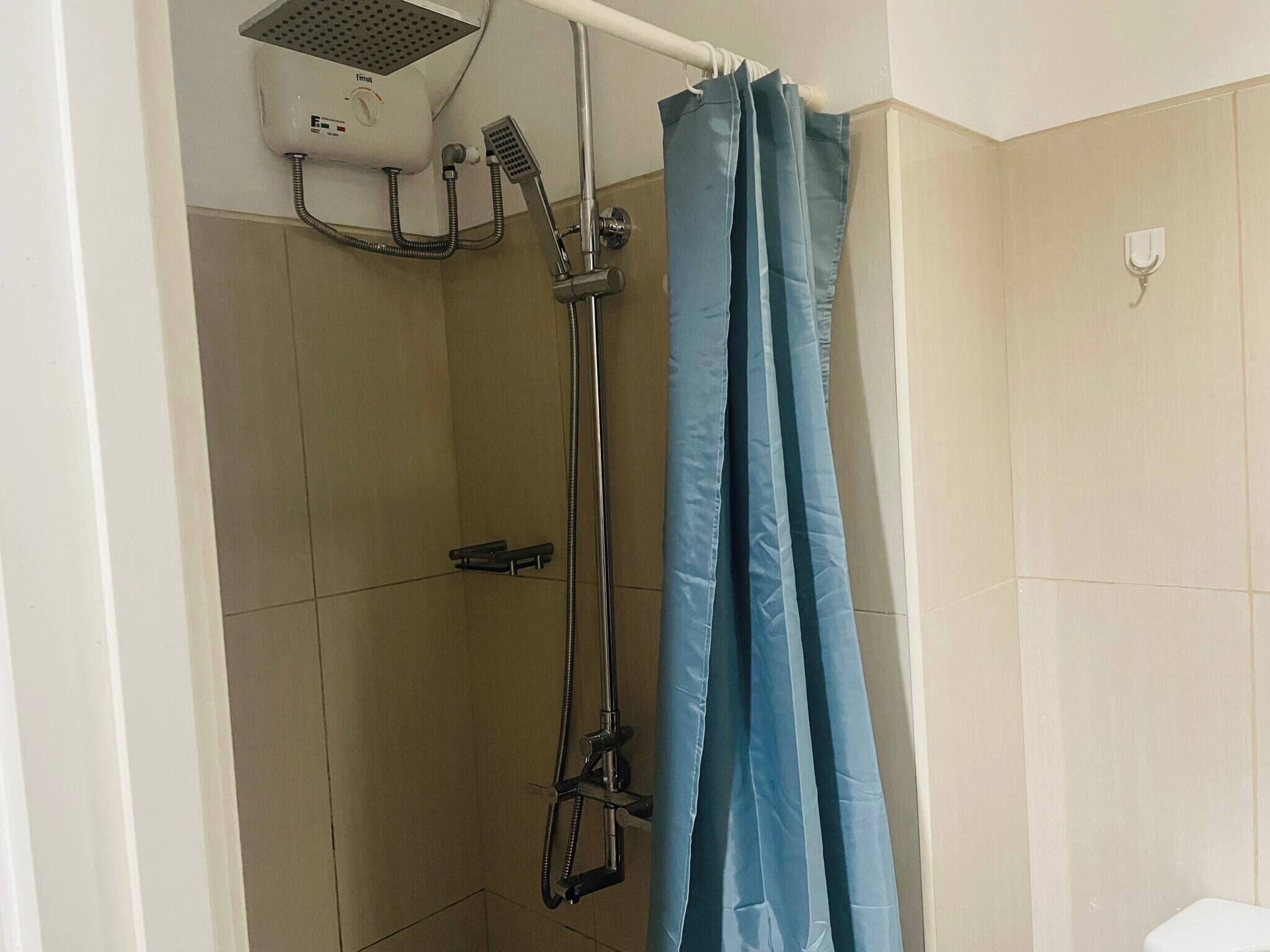 A shower area with a handheld showerhead, a wall-mounted hairdryer, and a blue shower curtain.