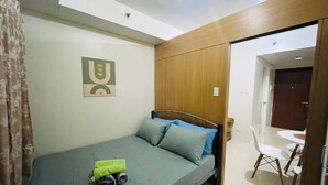 A single-bed room with a wooden headboard, a small table, and a chair. - Charming 1-bedroom Apartment Near Mall of Asia (Pasay)