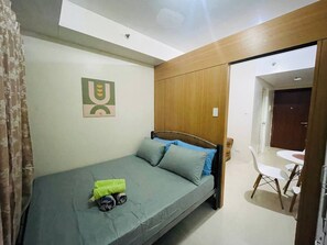 A single-bed room with a wooden headboard, a small table, and a chair. - Charming 1-bedroom Apartment Near Mall of Asia (Pasay)