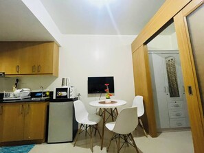 A compact kitchen with a refrigerator, microwave, and a small dining table with chairs. - Charming 1-bedroom Apartment Near Mall of Asia (Pasay)