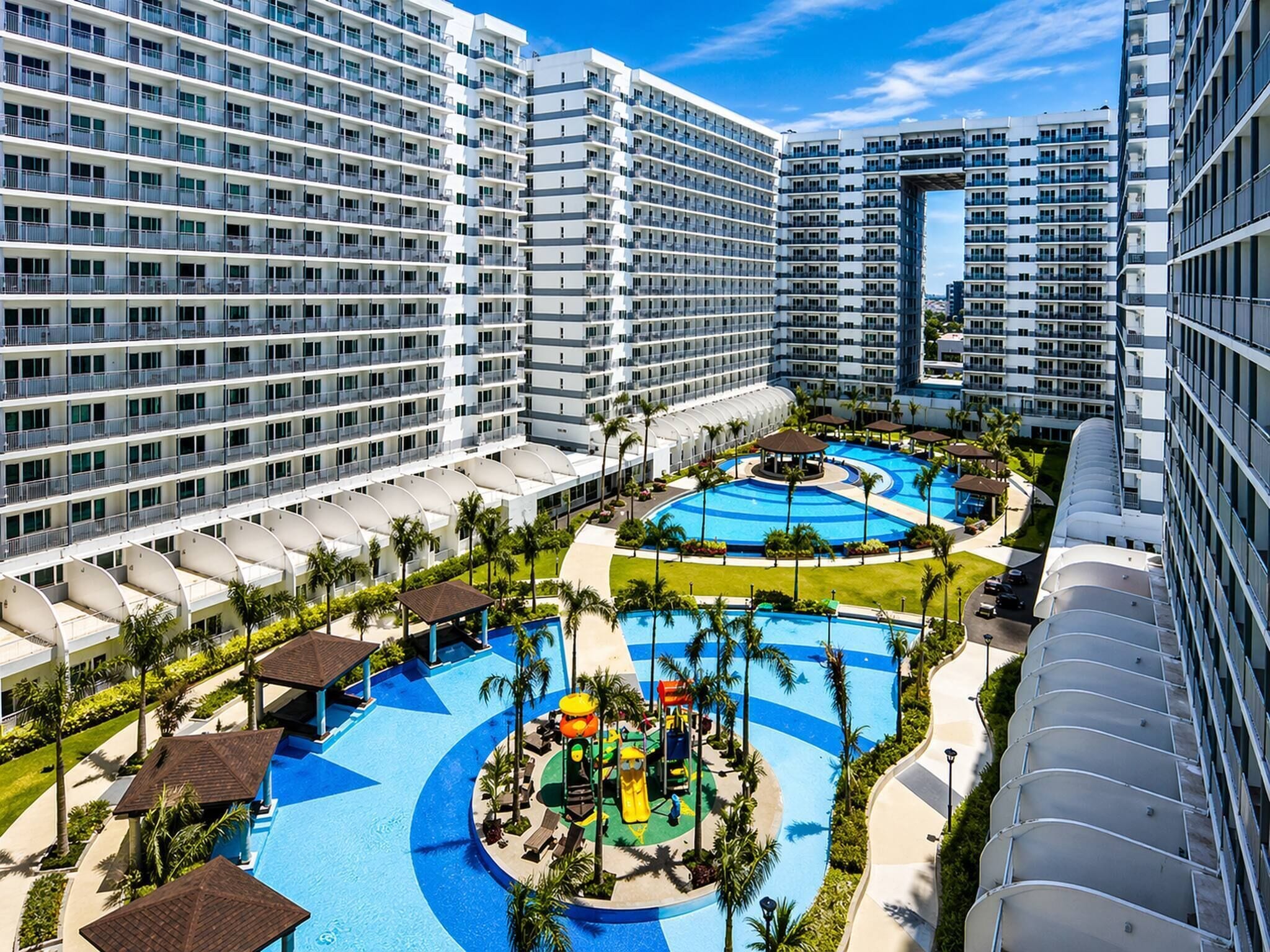 A high-rise hotel with multiple balconies, a central swimming pool, and a children's play area.