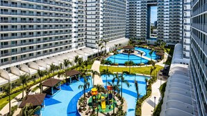 A high-rise hotel with multiple balconies, a central swimming pool, and a children's play area. - Charming 1-bedroom Apartment Near Mall of Asia (Pasay)
