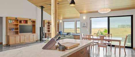 A modern kitchen with a large island, wooden cabinetry, and a view of a field through large windows.