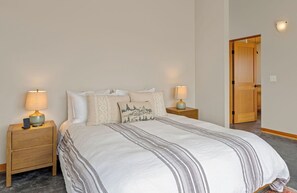 A bedroom with a bed, two bedside tables with lamps, a door, and a wall-mounted light fixture. - Driftwood Retreat | A Mindful Coastal Haven with Ocean Views & Hot Tub (The Sea Ranch)