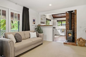 Ein modernes Wohnzimmer mit einem beigefarbenen Sofa, einem Kamin und einer Küche im Hintergrund.