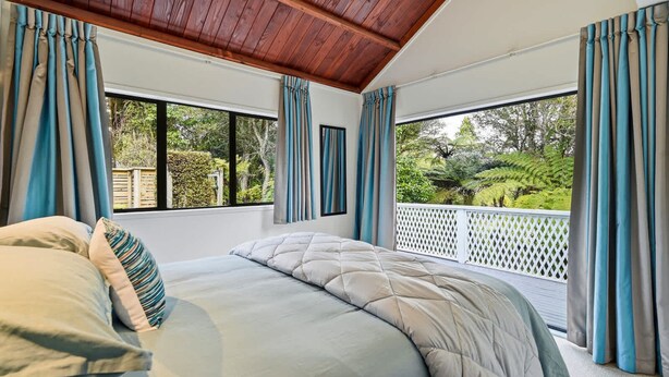 A bedroom with a large bed, a view of the outdoors through a window, and a wooden ceiling. - Tui Cottage - Walk to the Kaituna River (Okere Falls)