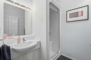 Une salle de bain avec un lavabo blanc, un miroir et une porte de douche.