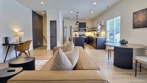 A modern living room with a sofa, a coffee table, and a dining area with a round table. - Upscale Stay, Free Parking, Walk to Eats and Parks (Birmingham)