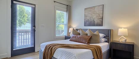 Une chambre à coucher comprenant un lit, des tables de chevet, un ventilateur de plafond et une fenêtre avec des stores.