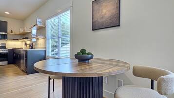 A modern kitchen with built-in appliances, a dining area with a round table, and a large window providing natural light.