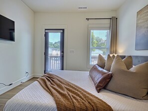 Ein Schlafzimmer mit einem Bett, einem an der Wand befestigten Fernseher und einem Fenster mit Jalousien.
