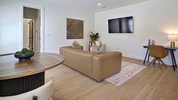 A modern living room with a round dining table, a sofa, a TV mounted on the wall, and a small desk with a lamp. - Upscale Stay, Free Parking, Walk to Eats and Parks (Birmingham)
