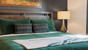A hotel room with a bed, green bedding, a headboard, a lamp, and a framed picture on the wall. - Fairway Lodge+Hot Tub+Golf+Sunset+Resort Pools (Hollister)