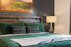 A hotel room with a bed, green bedding, a headboard, a lamp, and a framed picture on the wall. - Fairway Lodge+Hot Tub+Golf+Sunset+Resort Pools (Hollister)
