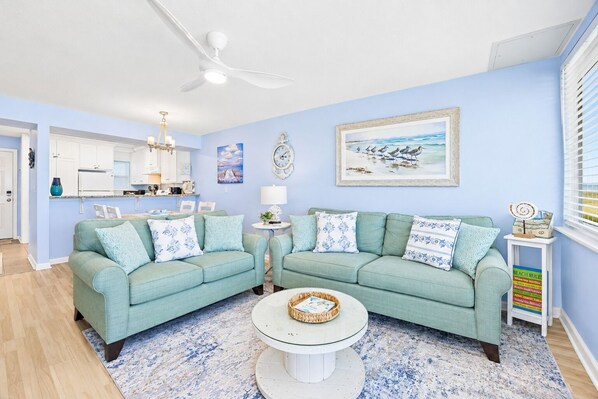 A living room with a light blue sofa set, a round coffee table, and a kitchen in the background. - Ocean-view 2BR condo in North End Fernandina Beach. (Fernandina Beach)