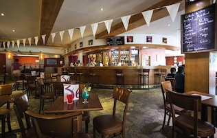 A restaurant with a bar area, wooden tables, and chairs.