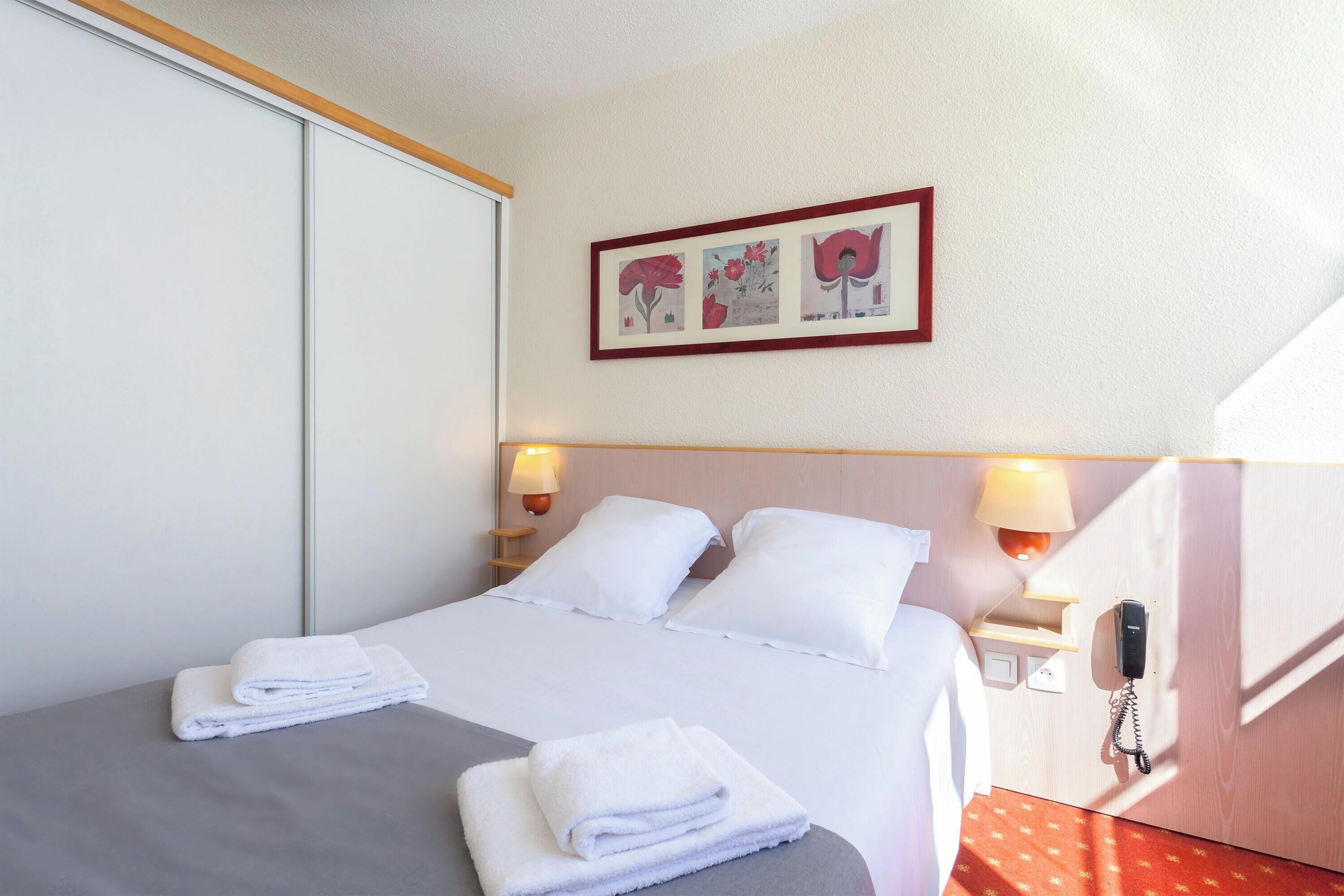 Habitación de hotel con cama, dos lámparas de noche, un teléfono y una obra de arte colgada en la pared.