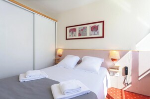 A hotel room with a bed, two bedside lamps, a telephone, and a wall-mounted artwork.