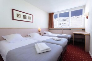 Une chambre d’hôtel avec deux lits, un bureau, une fenêtre donnant sur des montagnes enneigées et des tableaux encadrés accrochés au mur.