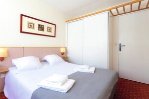 Habitación de hotel con cama, dos almohadas, mesita de noche con lámpara, un cuadro en la pared y una puerta cerrada.