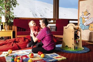 A room with a child playing, a wooden play structure, and a large window with a snowy mountain view.