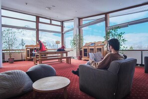 A spacious room with large windows, a wooden bench, a sofa, and a table. - Club Belambra Les Menuires Neige & Ciel (Les Belleville)