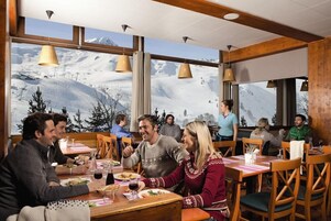 A restaurant with wooden furniture and large windows offering a view of a snowy mountain landscape.
