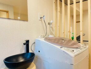 A washing machine with a lid, a black basin, and a power outlet on the wall. - SERENE | Nishikujo, 4th Floor | 60 ㎡, Sleeps 7 | Direct Access to USJ and Osaka Station (大阪市)