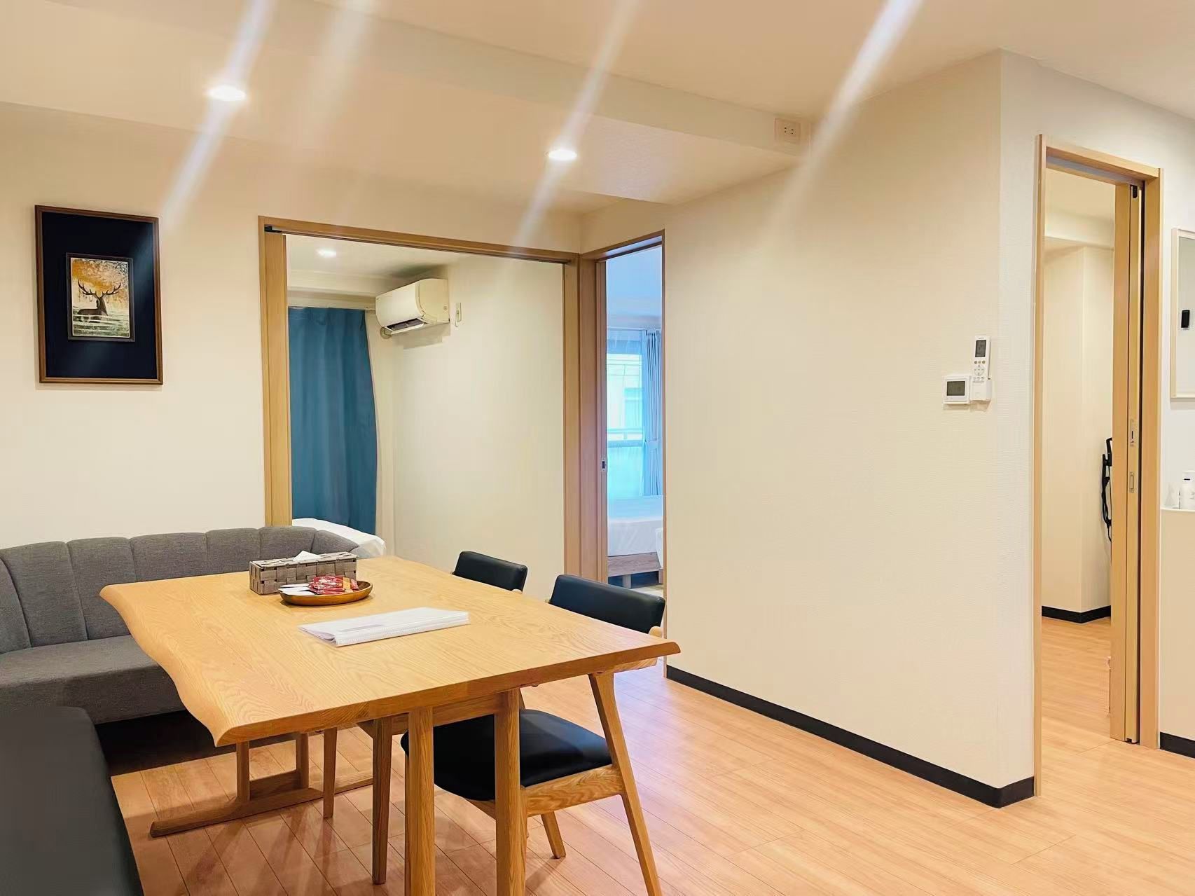Une pièce comprenant une table à manger en bois, un canapé gris et un grand miroir qui reflète une fenêtre avec des rideaux.