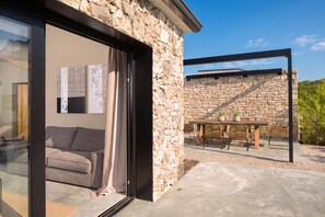 A modern stone building with a glass door leading to a living area with a sofa and a table with chairs. - Villa Iron Lady Labin – Private Pool & Sea View, Labin, Croatia (Labin)