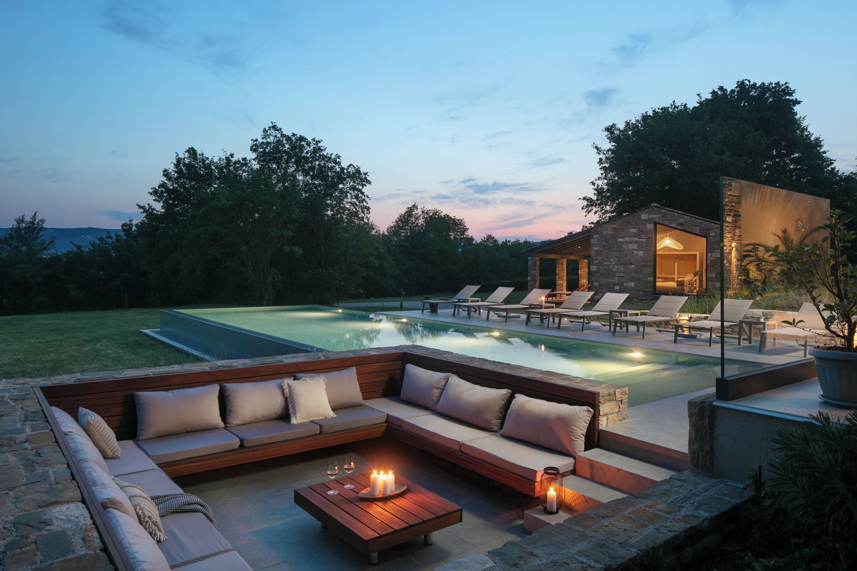 Un espace aménagé au bord de la piscine, doté d’un coin salon intégré, d’une structure en pierre et offrant une vue sur le paysage environnant.