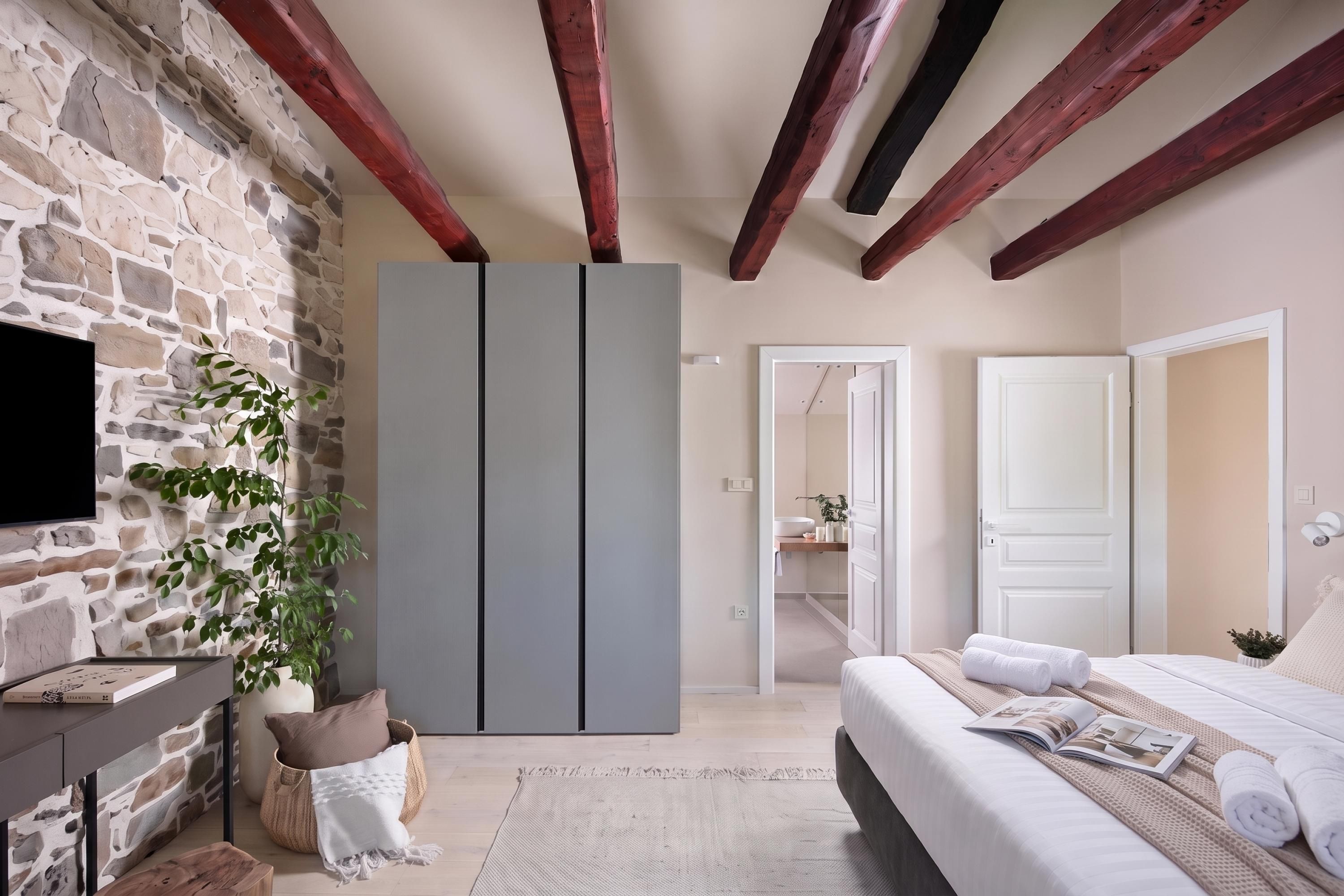 Een slaapkamer met een stenen muur, een bed met wit beddengoed, een grijze garderobe en een televisie aan de linkerkant.