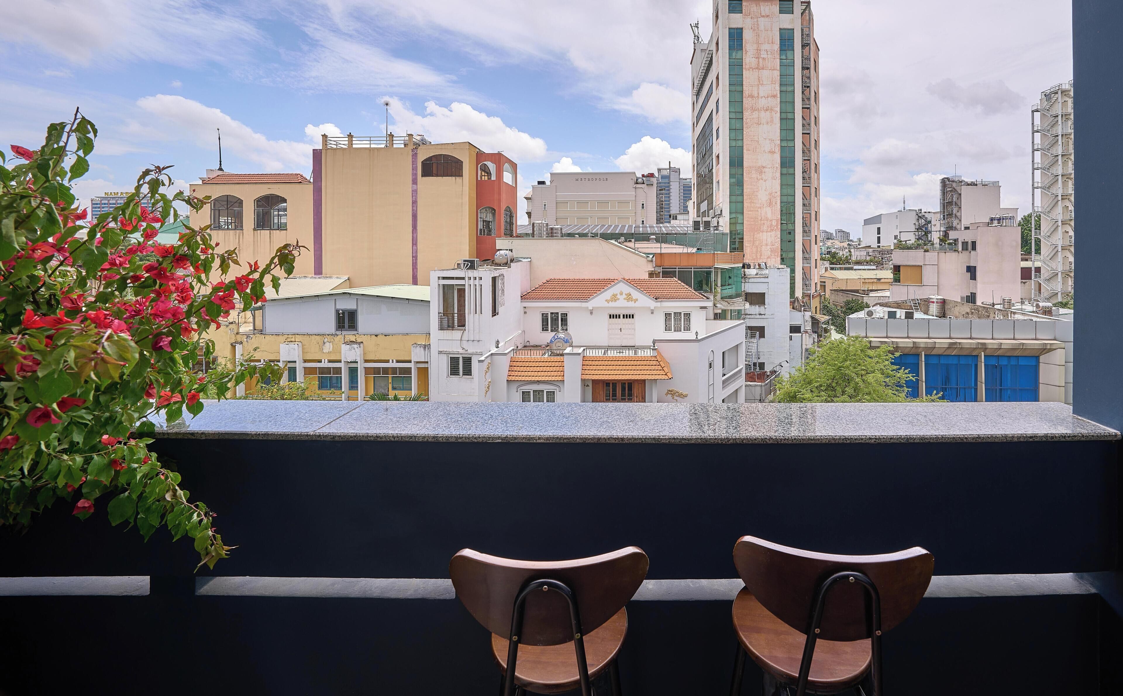 Un balcon avec deux chaises en bois, donnant sur un paysage urbain composé de différents bâtiments, dont une haute structure portant l’inscription « METROPOLIS ».
