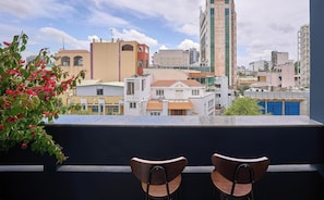 A balcony with two wooden chairs, overlooking a cityscape with various buildings, including a tall structure labeled 'METROPOLIS.' - Cubicity Ba Huyen Thanh Quan (Ho Chi Minh City)