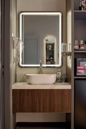 A bathroom with a large mirror, a white sink, a telephone, and a shelf with toiletries. - Cubicity Ba Huyen Thanh Quan (Ho Chi Minh City)