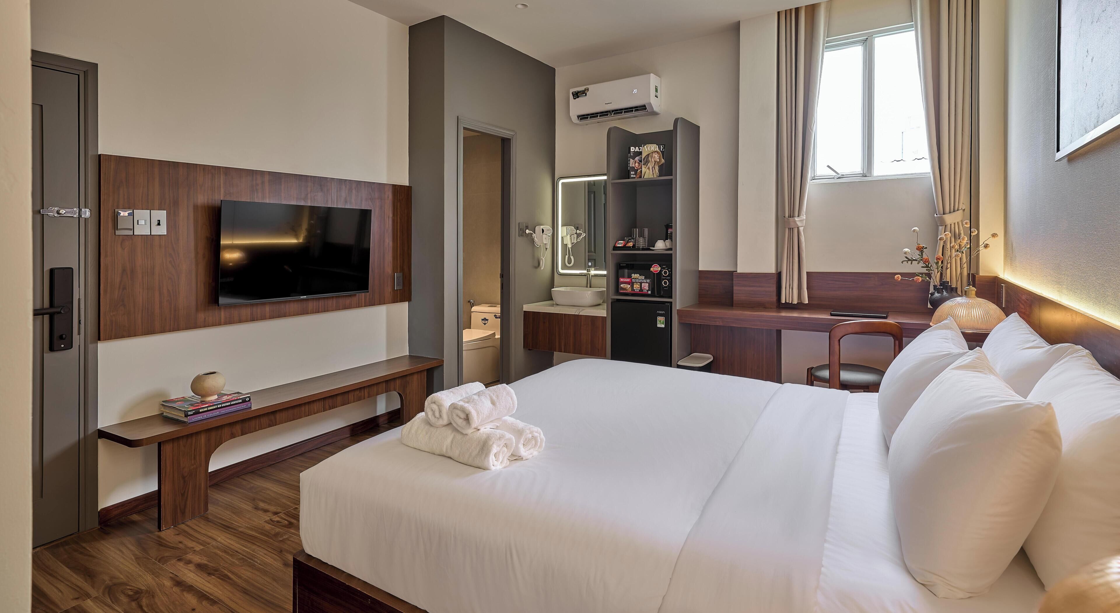 A hotel room with a bed, a desk, a television, a bathroom, and an air conditioning unit.