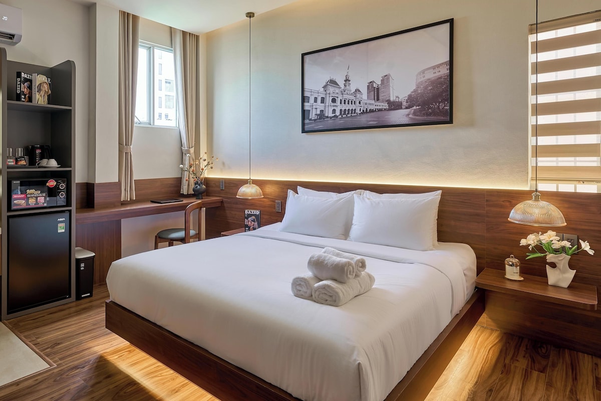 A hotel room with a bed, bedside table, lamp, and a large window.