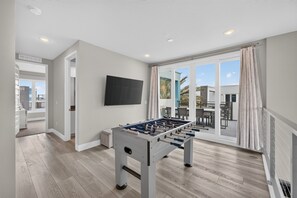 A modern room with a foosball table, a flat-screen TV, and a sliding glass door leading to an outdoor area. - Reunion Resort 5BR Condo | Park View | Resort Pool (Kissimmee)