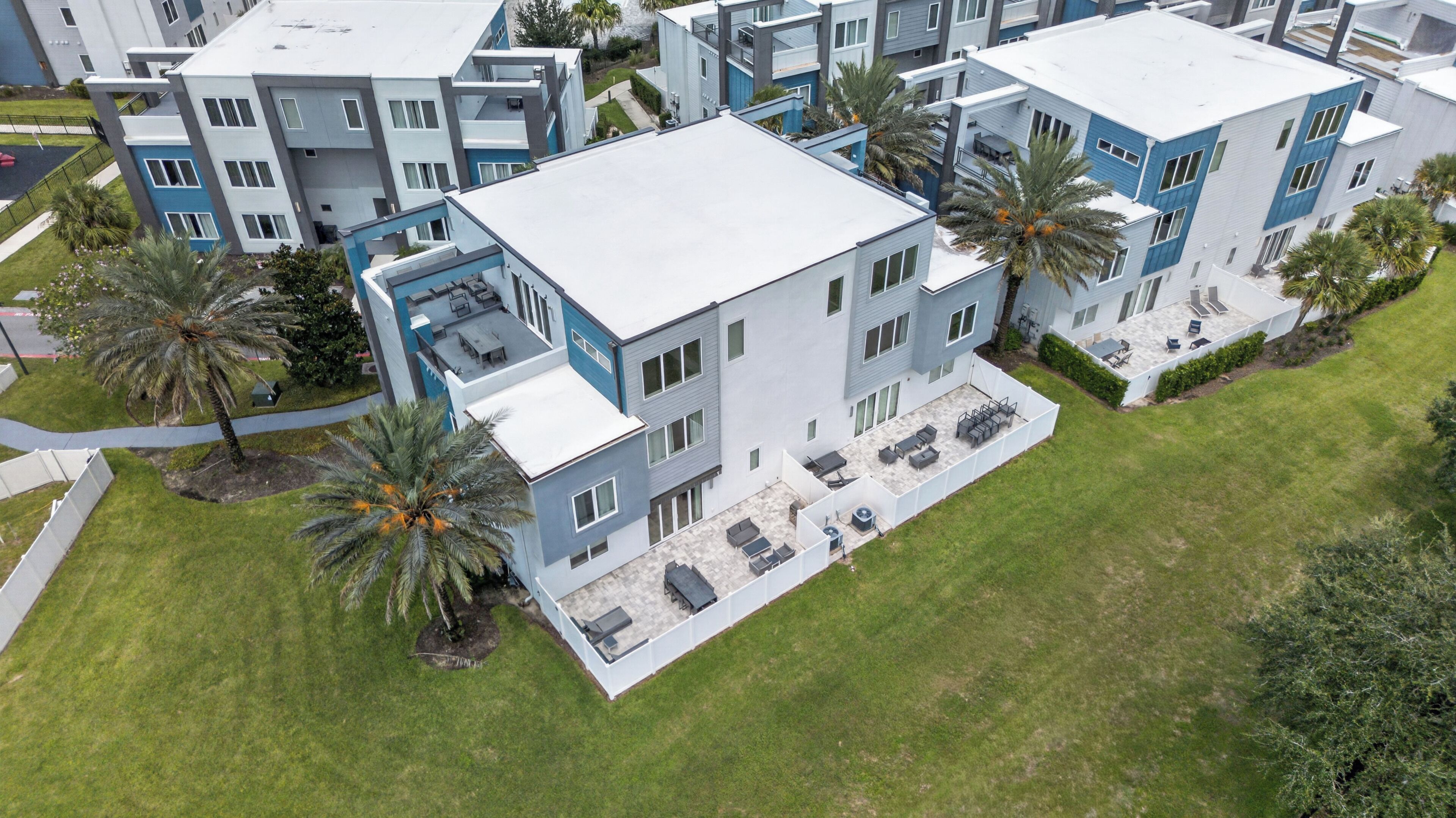 A modern multi-story residential building with a flat roof, large windows, and a covered outdoor patio area.