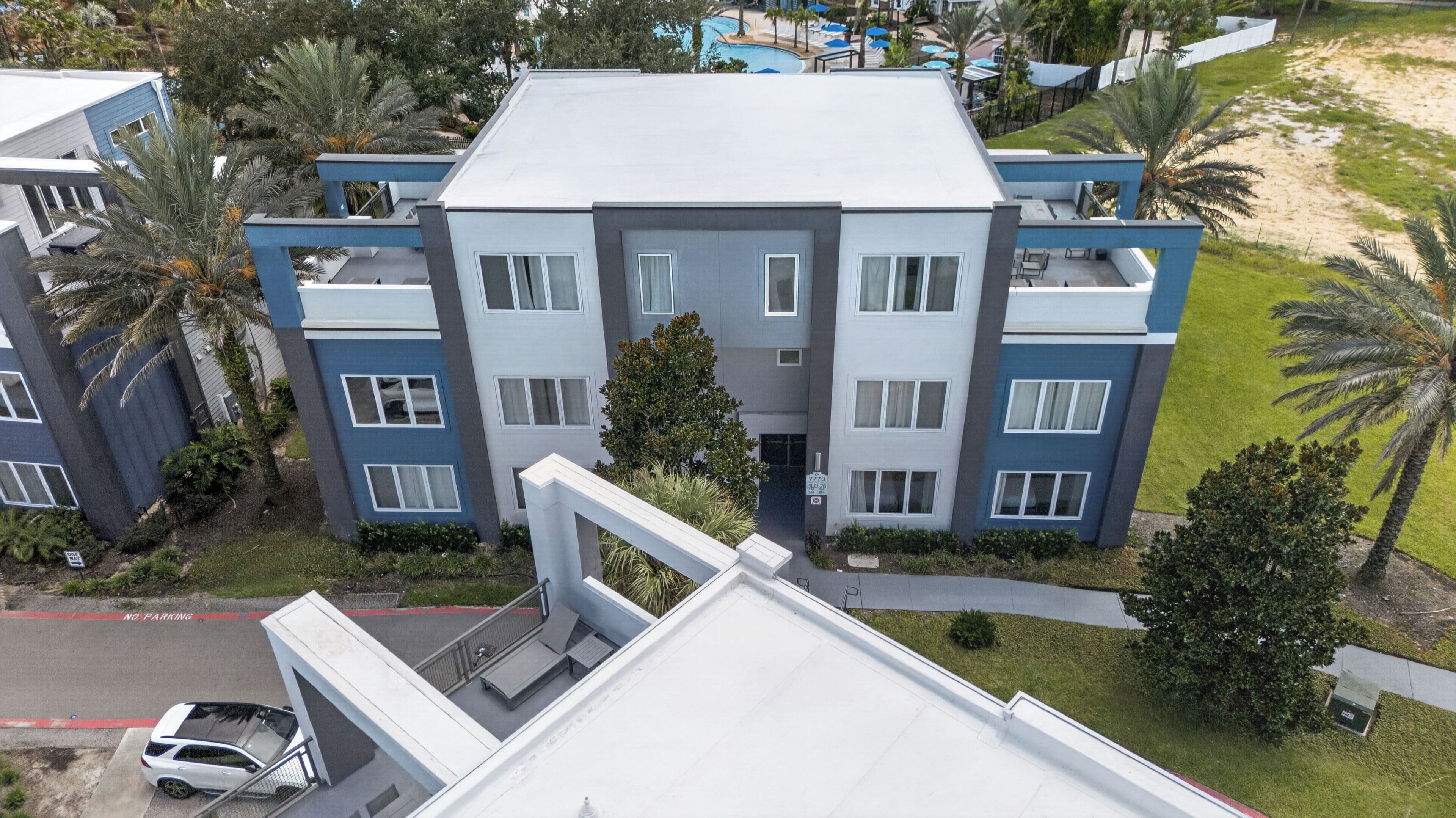 A multi-story building with balconies, a swimming pool, and a parking area.