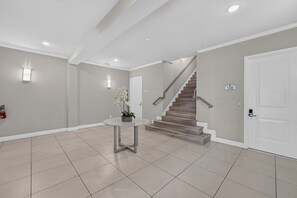 A clean, modern lobby with a staircase, a small table with a plant, and a fire extinguisher on the wall. - Reunion Resort 5BR Condo | Park View | Resort Pool (Kissimmee)