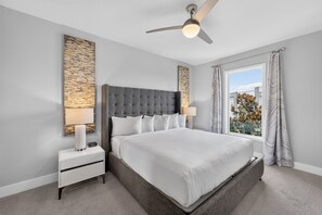 A modern bedroom with a large bed, a ceiling fan, and a window with curtains. - Reunion Resort 5BR Condo | Park View | Resort Pool (Kissimmee)
