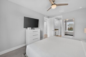 A bedroom with a bed, a TV mounted on a dresser, a ceiling fan, and a bathroom visible through an open door. - Reunion Resort 5BR Condo | Park View | Resort Pool (Kissimmee)