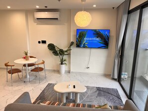 A modern room with a round table, chairs, a potted plant, a flat-screen TV, and a large window.