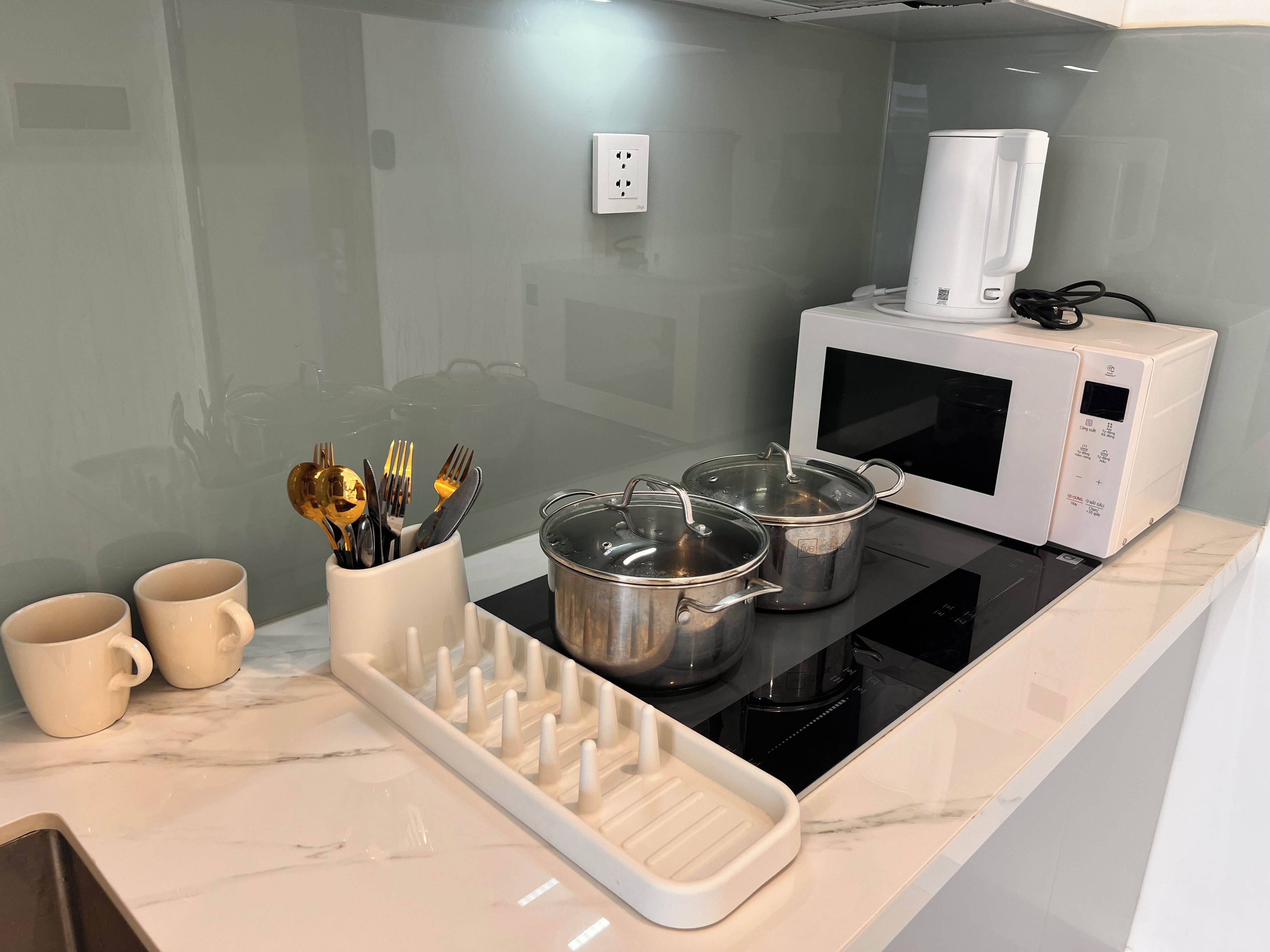 A kitchen with a microwave, pots on the stove, a utensil holder, and two mugs on the counter.